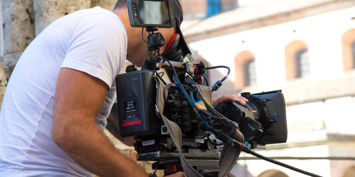Behind the scene. Video camera operator (cameraman) filming movie scene on outdoor location. Detail of professional camera equipment. Italy, Urbino